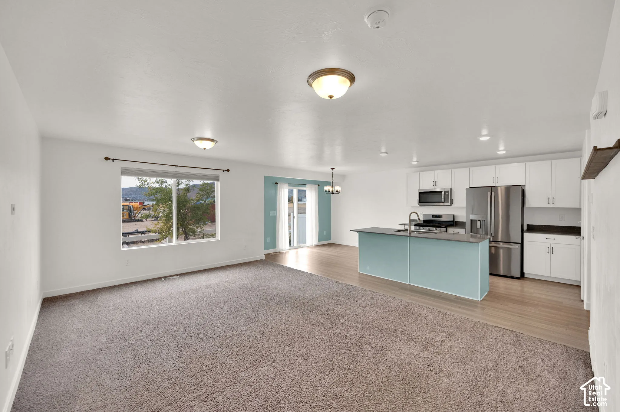 Open-concept interior featuring a kitchen with white cabinetry, a kitchen island, stainless steel appliances, wood-finish flooring, and wall-to-wall carpeting