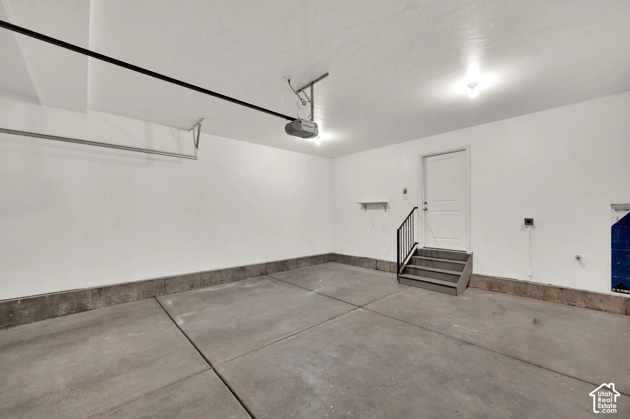 Finished garage with smooth concrete flooring, white walls, automated door opener, and interior access door with metal handrail