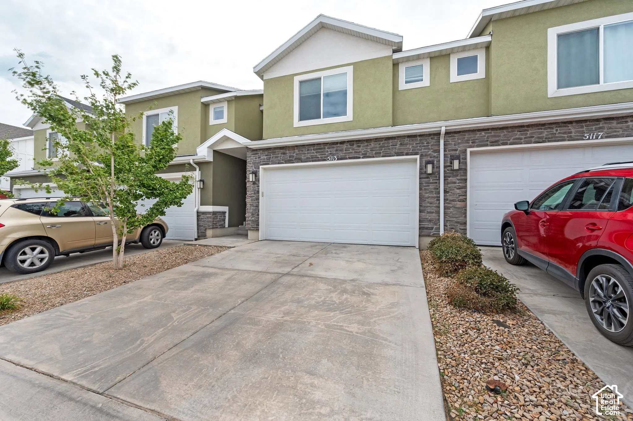 Multi-level exterior featuring stone veneer accents, stucco siding, a concrete driveway, and an attached two-car garage