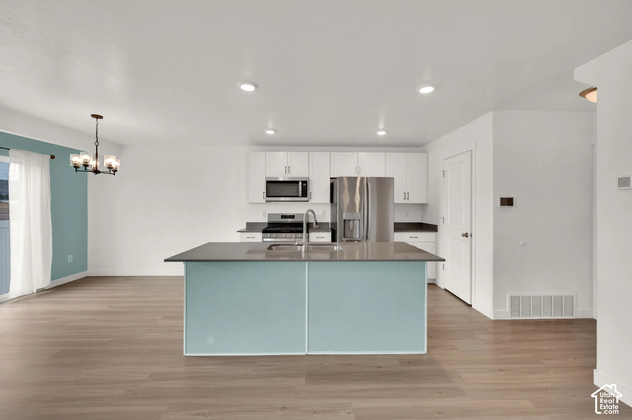 Kitchen featuring white flat-panel cabinetry, stainless steel appliances, a center island with a solid-surface countertop, and wood-finish flooring