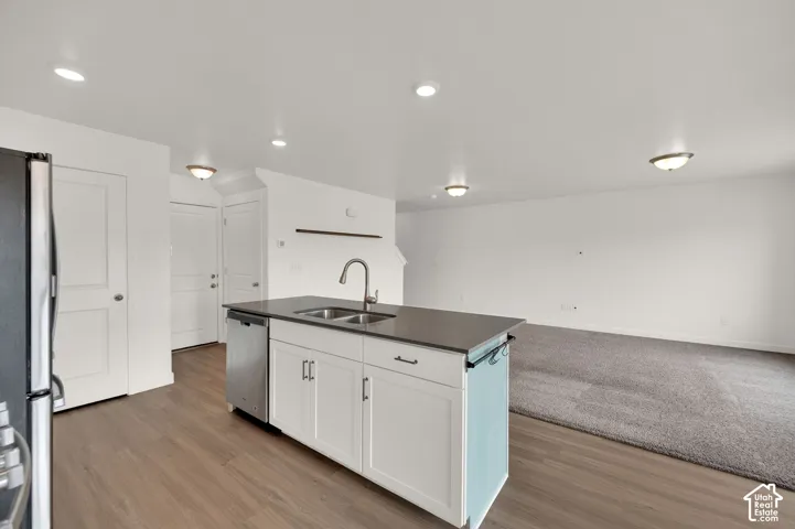Kitchen island featuring a dark countertop, white shaker-style cabinetry, a stainless steel dishwasher, and a gooseneck faucet, set against wood-finish flooring