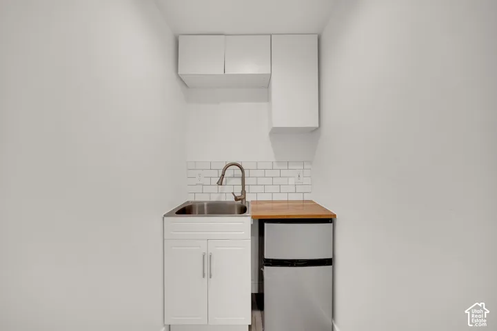 Built-in kitchenette featuring white cabinetry, subway tile backsplash, stainless steel drop-in sink, wood-finish countertop, and wall-mounted storage cabinets
