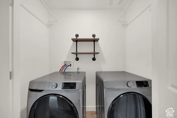 Laundry alcove featuring white walls, dual overhead clothing rods, and wall-mounted shelving with wood-finish planks and dark metal piping supports