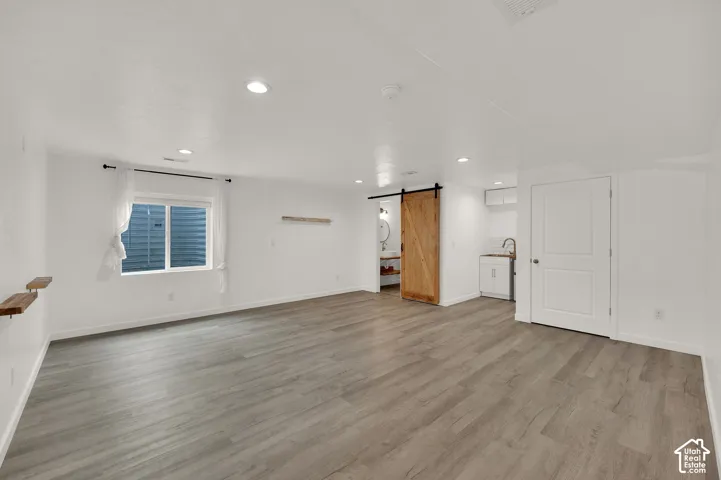 Open-concept room featuring wood-finish flooring, recessed lighting, a sliding barn-style door, and a built-in kitchenette with cabinetry and a sink