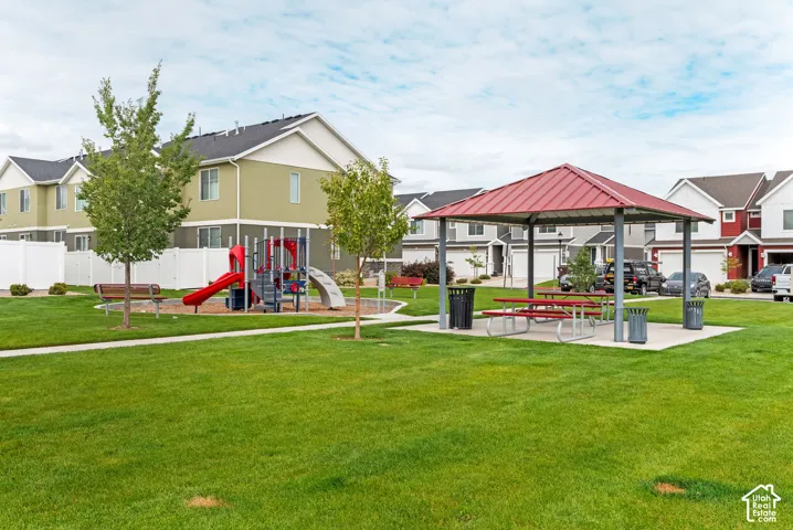 Community recreation area featuring a pavilion with a metal roof, picnic tables, play structure, manicured lawn, and mature trees