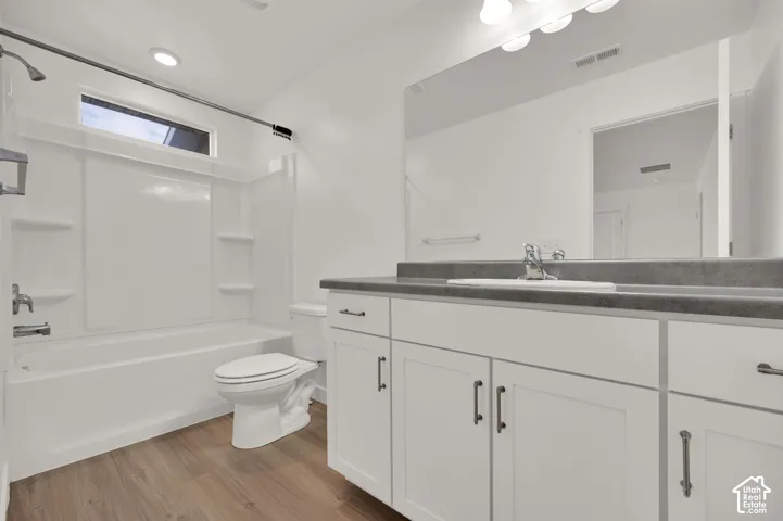 Bathroom featuring a white vanity with a dark solid-surface countertop, an integrated sink, an oversized wall-mounted mirror, wood-finish flooring, and a tub-shower combination with built-in shelving