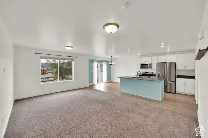 Open-concept interior featuring a kitchen with white cabinetry, a kitchen island, stainless steel appliances, wood-finish flooring, and wall-to-wall carpeting