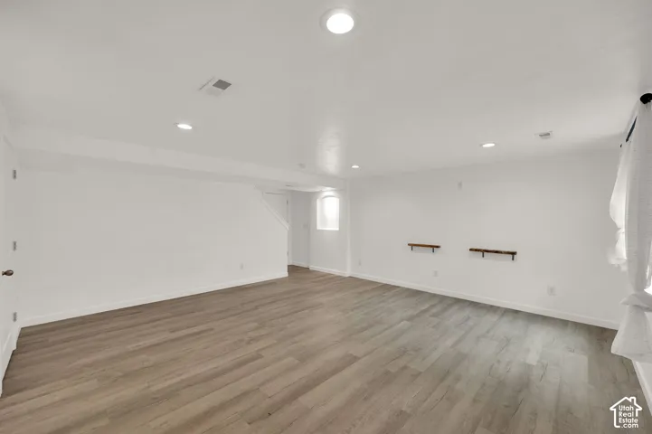 Open-concept room featuring wood-finish flooring, recessed lighting, built-in wall niche, and two wall-mounted wood shelves