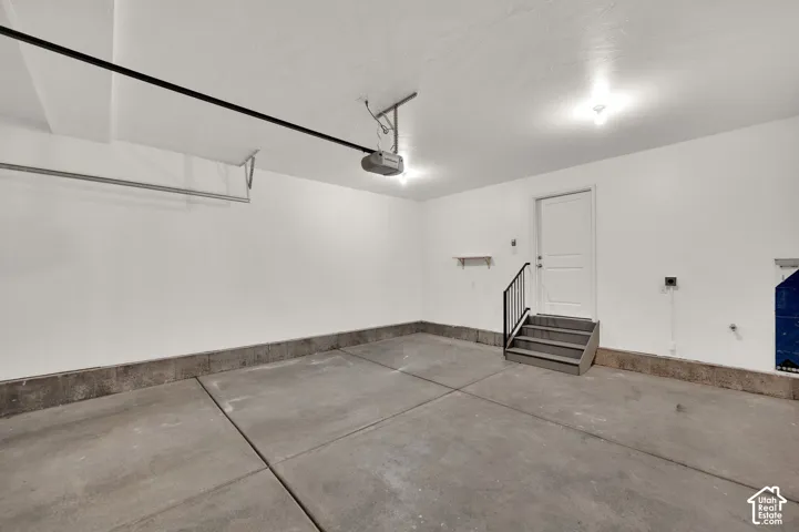 Finished garage with smooth concrete flooring, white walls, automated door opener, and interior access door with metal handrail