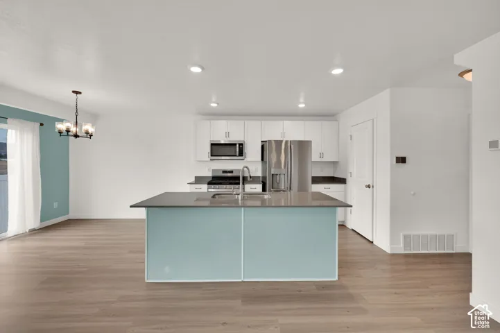 Kitchen featuring white flat-panel cabinetry, stainless steel appliances, a center island with a solid-surface countertop, and wood-finish flooring