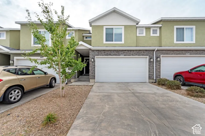 Multi-level exterior featuring stucco siding, stone veneer accents, concrete driveway, two-car garage, and gable roofline
