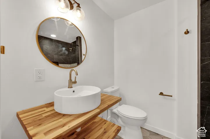 Bathroom featuring a dual-level butcher block vanity, white vessel sink with a brass-finish faucet, oval gold-rimmed mirror, and light fixture with clear glass shades