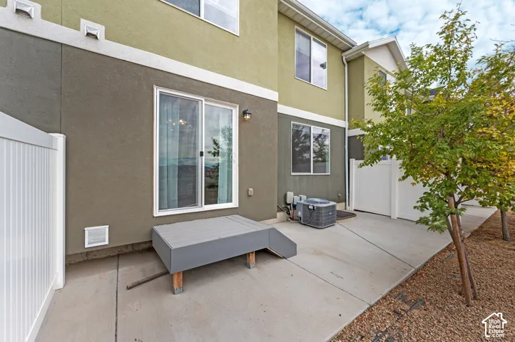 Exterior patio featuring a concrete slab, low-profile composite step, dual-tone stucco siding, white vinyl privacy fencing, and exterior wall-mounted lighting