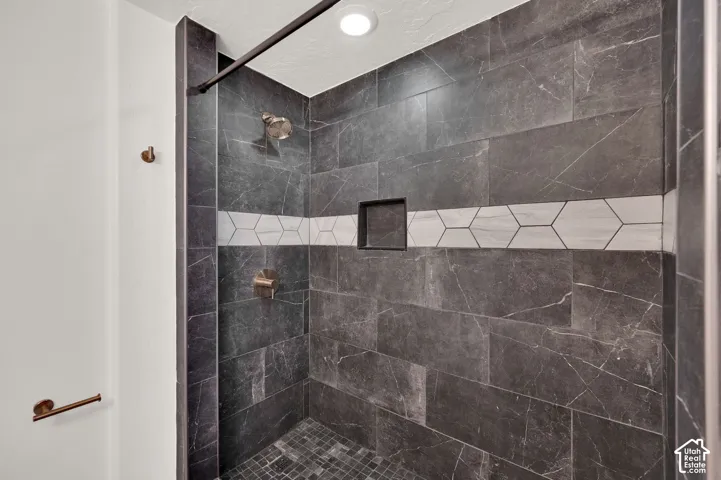 Shower stall featuring large-format dark charcoal tile, a contrasting white hexagonal tile accent band, integrated recessed storage niche, pebble-style floor tiling, and a metallic shower fixture