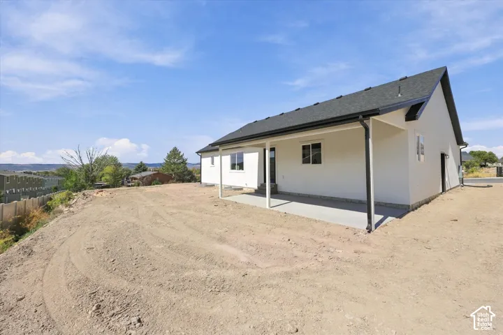 Single-story residence featuring a smooth stucco exterior, dark shingle roof, integrated covered patio, and wide-set windows