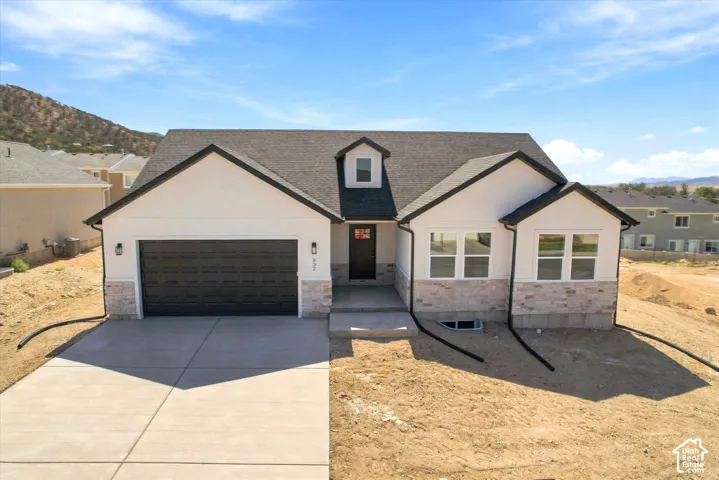 Single-story exterior featuring a multi-gable roofline, neutral-toned stone veneer accents, stucco siding, and a two-car garage