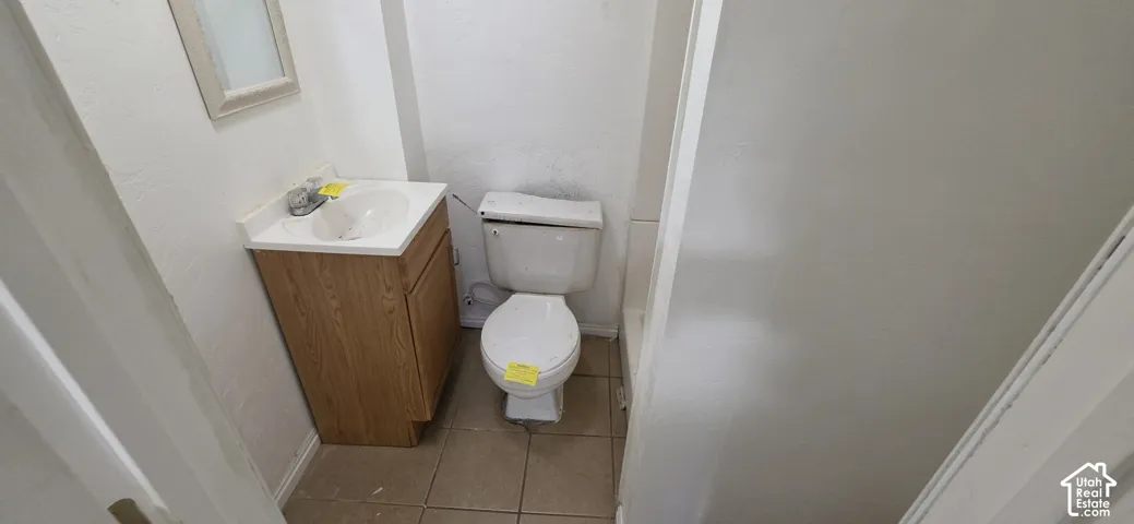 Bathroom featuring a wood-finish vanity with a white countertop, ceramic sink, tiled flooring, and a porcelain toilet