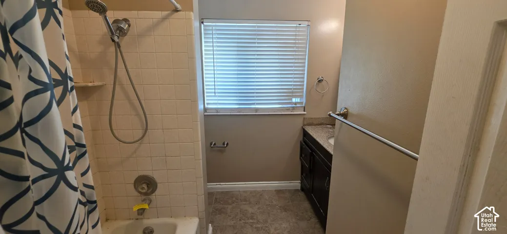 Bathroom featuring a vanity with stone-finish countertop, shower-tub combination with tile surround, handheld showerhead, and window with horizontal blinds