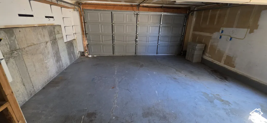Two-car garage featuring a sectional metal door, concrete flooring, exposed concrete wall sections, and built-in wall-mounted hooks