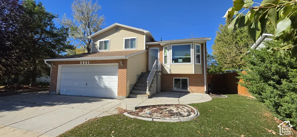 Split-level exterior featuring vinyl siding, brick masonry, an attached two-car garage, a concrete driveway, and a front bay window
