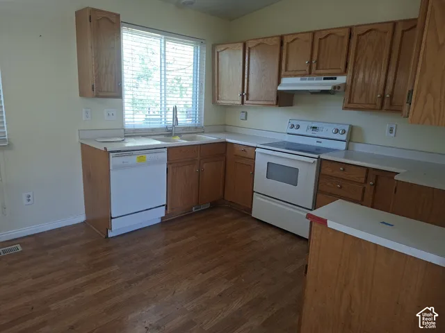 Kitchen featuring wood cabinetry, white countertops, wood-finish flooring, a stainless steel kitchen faucet, and built-in white appliances