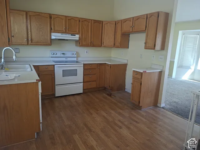 Kitchen featuring wood-finish cabinetry, white solid-surface countertops, white electric range, and wood-finish flooring