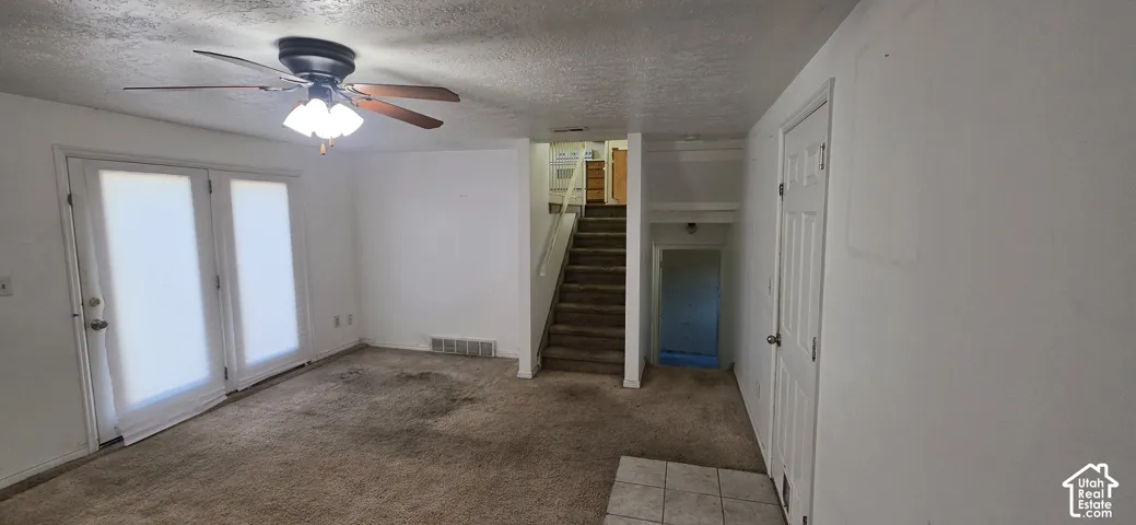 Interior space featuring carpeted flooring, a ceiling-mounted light fixture with fan, double glass-pane doors, and a staircase