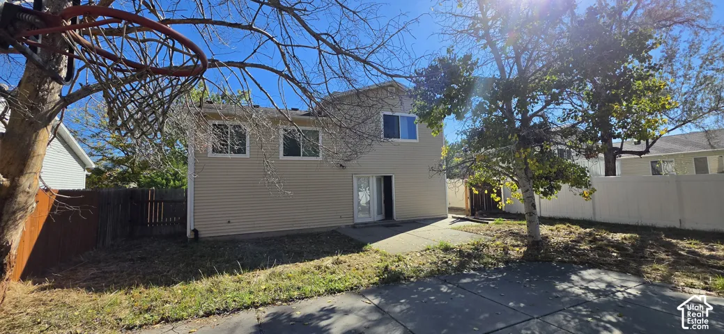 Exterior rear elevation featuring beige horizontal siding, a concrete patio, and a perimeter privacy fence