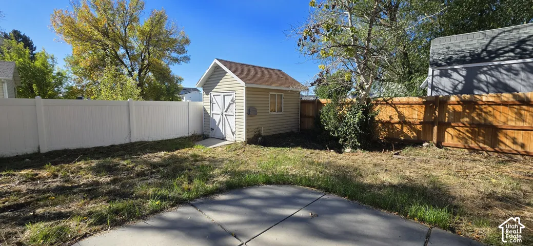 Backyard featuring a detached storage shed, concrete patio, white vinyl fencing, and natural wood-finish privacy fencing
