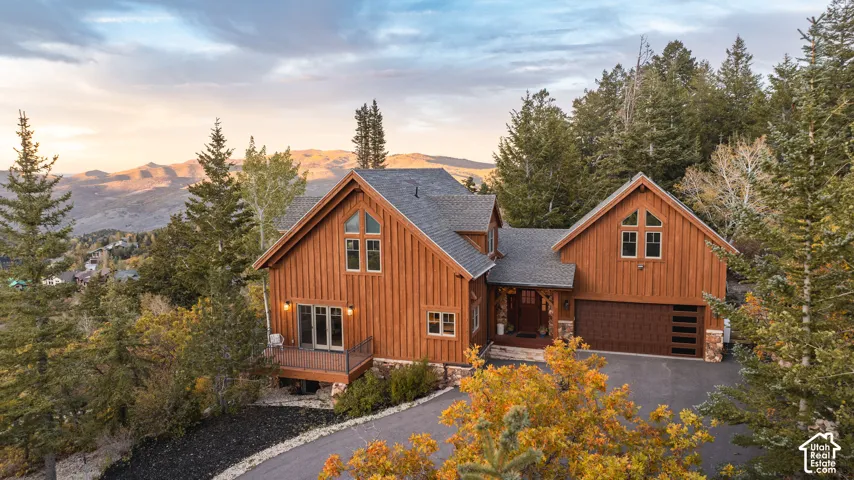 Multi-level residence featuring board and batten siding, stone foundation accents, multi-pane windows, attached multi-car garage, and an elevated exterior deck