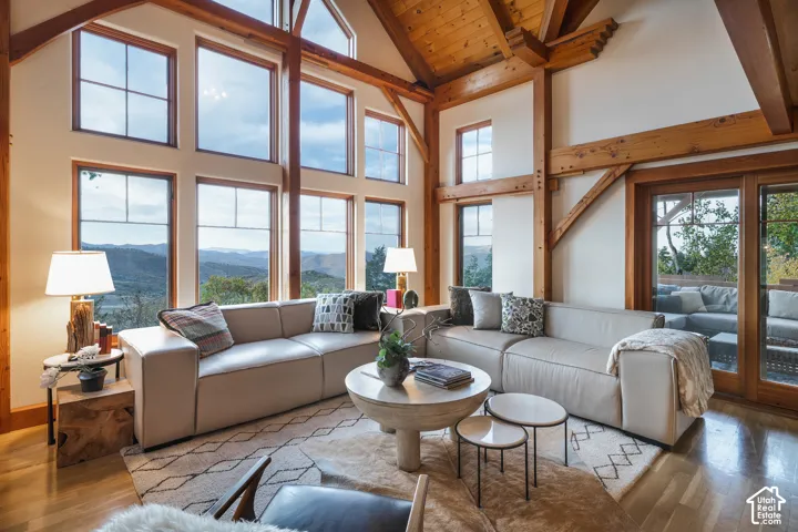 Vaulted ceiling with exposed timber framing, floor-to-ceiling multi-pane windows, wood-finish flooring, and glass-paneled exterior doors