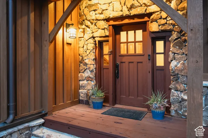 Covered entrance featuring heavy timber framing, stacked stone facade, natural wood board-and-batten siding, and a solid wood door with vertical glass panes