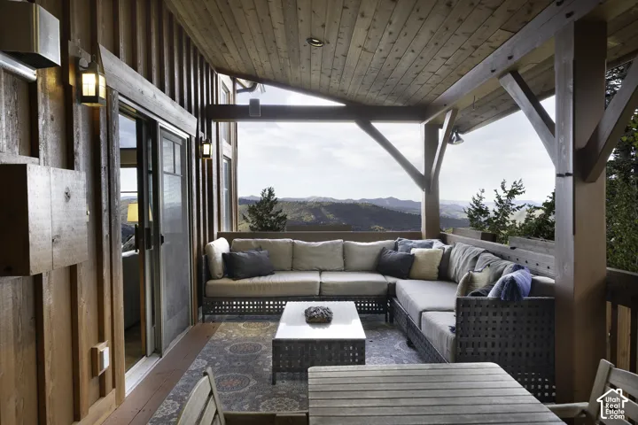 Covered deck featuring vertical wood siding, a tongue-and-groove wood ceiling, exposed timber support beams, and mountain scenery