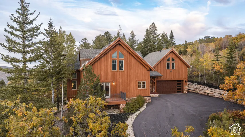 Mountain-style exterior featuring vertical wood siding, stone foundation accents, multi-gabled rooflines, oversized windows, and an integrated garage