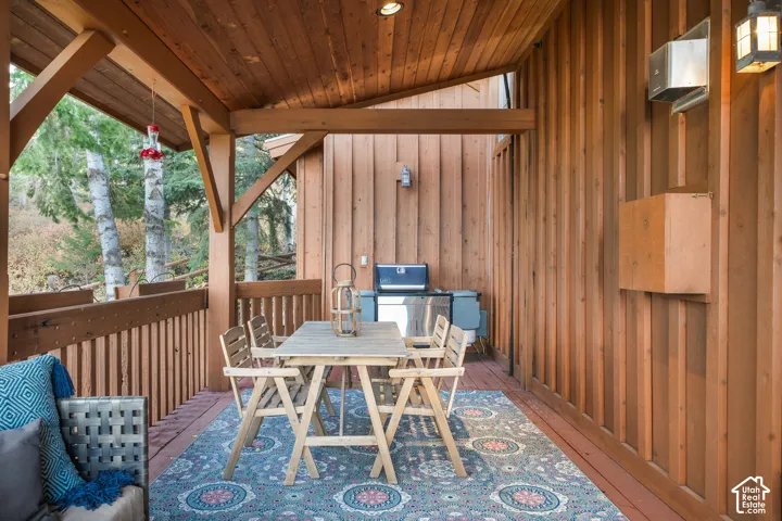 Covered wooden deck featuring vertical cedar siding, exposed timber framing, and a wooden railing