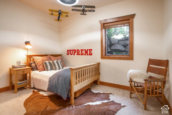 Room featuring natural wood-finish window trim, carpeted flooring, wall-mounted light fixture, and large rock-retaining wall exterior feature