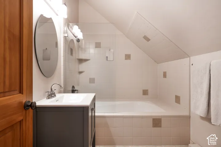 Bathroom featuring a dark gray vanity with a white countertop, a glass shower partition, a deep soaking tub, and tiled shower surround with decorative accent tiles