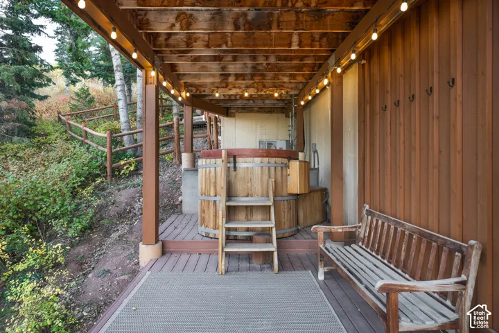 Covered outdoor deck featuring a wood-finish soaking tub, vertical wood siding, and integrated string lighting