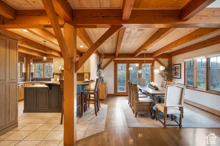 Exposed timber ceiling beams, wood-finish flooring, central kitchen island with stone countertop, natural wood ceiling planking, and multi-pane windows