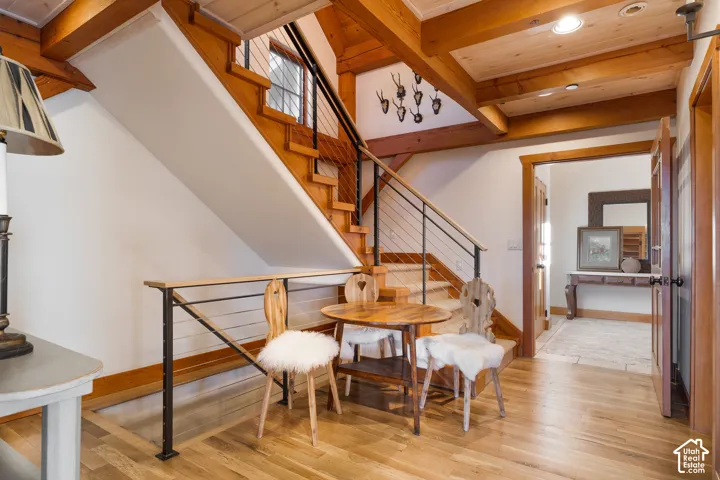Staircase featuring exposed timber beams, a horizontal cable railing system, and wood-finish treads, set against wood-finish flooring and plank-style ceiling accents