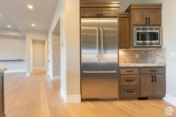 Modern kitchen featuring stainless steel French-door refrigerator with freezer drawer, custom wood cabinetry with brushed hardware, built-in microwave, brick backsplash, and wide-plank wood-finish flooring extending throughout the open layout