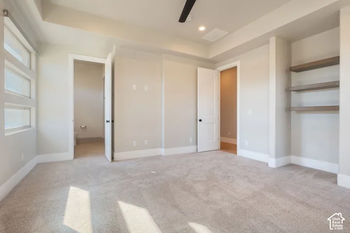 Recessed ceiling with integrated lighting, carpeted flooring, built-in shelving, white trim, and a ceiling fan