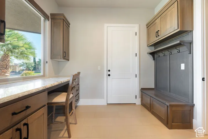 Built-in desk area with stone-finish countertop, wood-finish cabinetry, built-in storage bench, and integrated coat rack