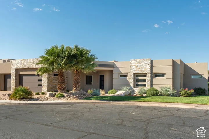 Contemporary stucco exterior with stone accents, a modern garage door, desert landscaping, and a manicured lawn