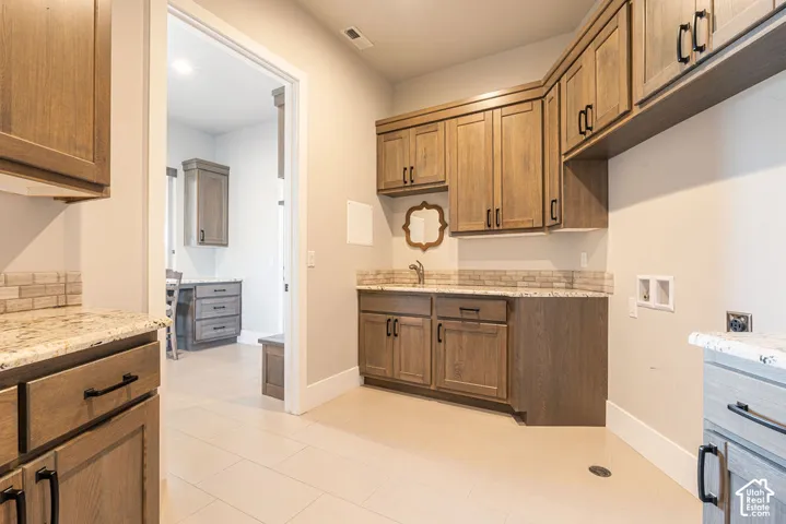 Galley kitchen featuring warm wood cabinetry with oil-rubbed bronze hardware, ceramic tile flooring, and stainless steel sink with integrated dishwasher