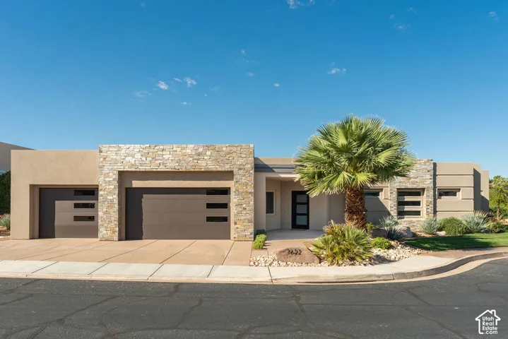 Contemporary stucco exterior with stone accents, featuring a two-car garage, single-car garage, and desert-inspired landscaping