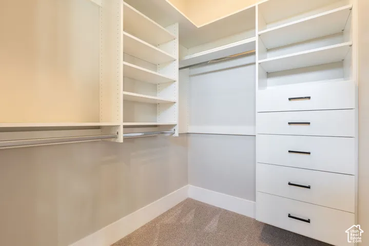 Spacious walk-in closet featuring custom white cabinetry with five deep drawers, open shelving along multiple walls, and neutral finish flooring