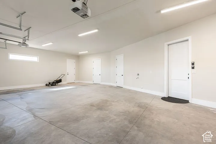 Spacious garage featuring polished concrete flooring, multiple white panel doors, recessed and linear ceiling lighting, and a garage door opener system