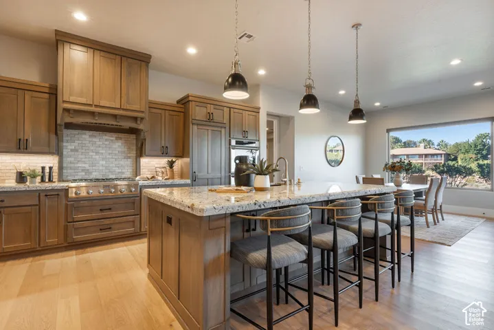 Kitchen featuring custom wood cabinetry, stone-surface central island, built-in range hood, stone tile backsplash, and wood-finish flooring
