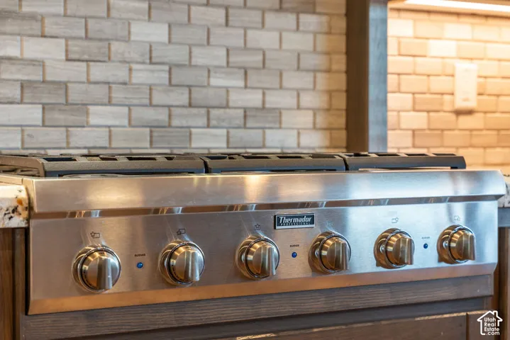 Stainless steel range with a Thermador brand visible, granite-finish countertop, and a brick-patterned backsplash